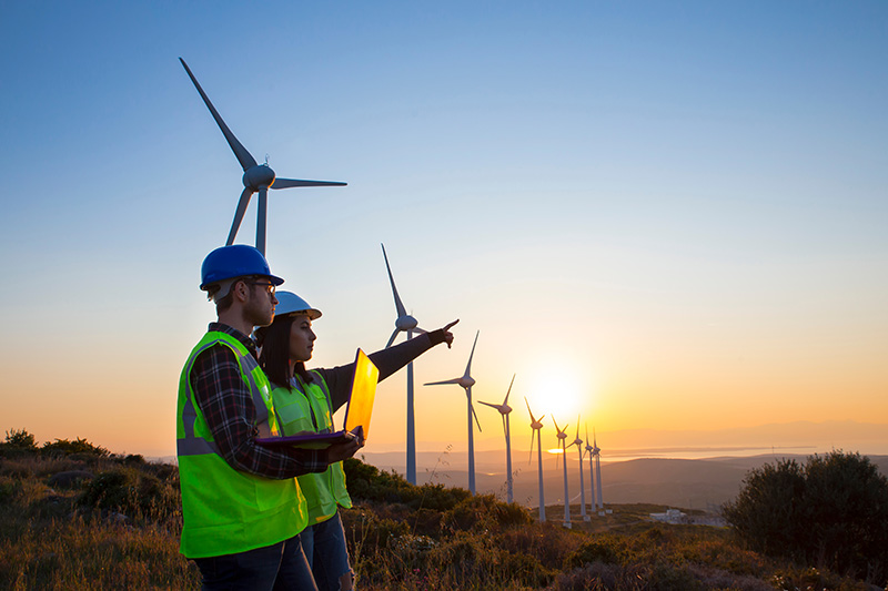 Two workers pointing with wind turbines in the background at sunset