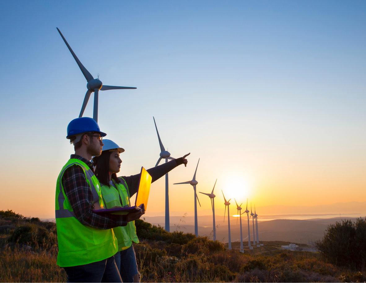 Two employees standing next to wind turbines at sunset